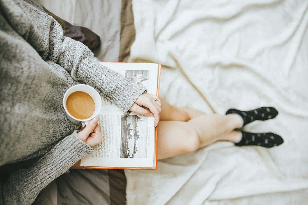 Photo of a single woman doing self care by drinking coffee and reading a book 