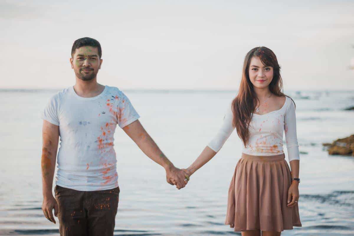 A masculine man and a feminine woman holding hands in front of the water